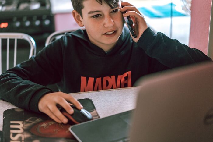 Teen in Marvel hoodie on a laptop and phone, illustrating creepiest displays of intelligence