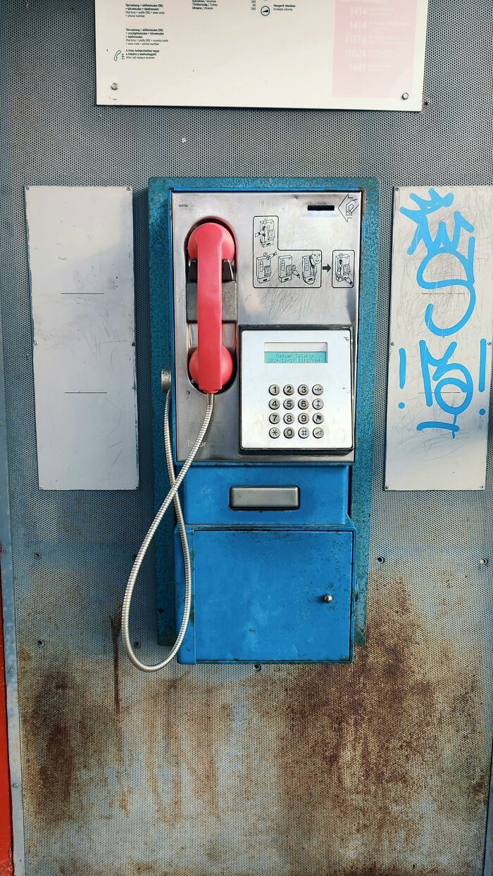 It Rained Frogs - weathered blue public payphone with red handset, graffiti and rusted metal background