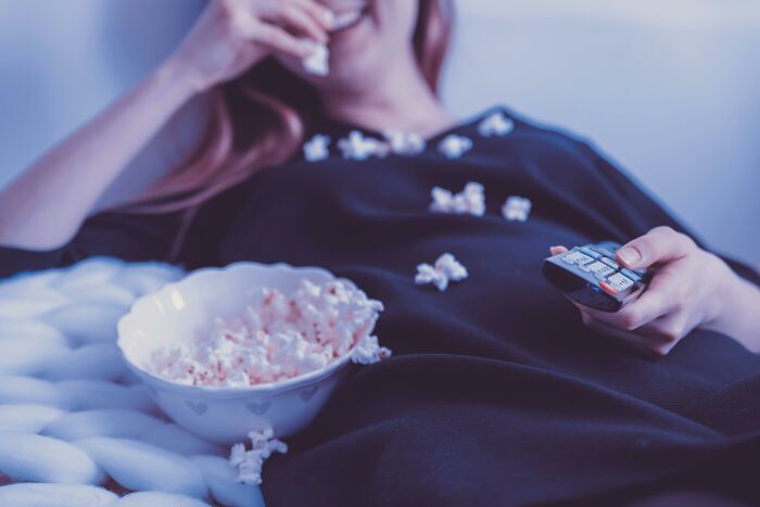 Person relaxing with popcorn and remote, watching movies and TV shows to decode funky synonyms.