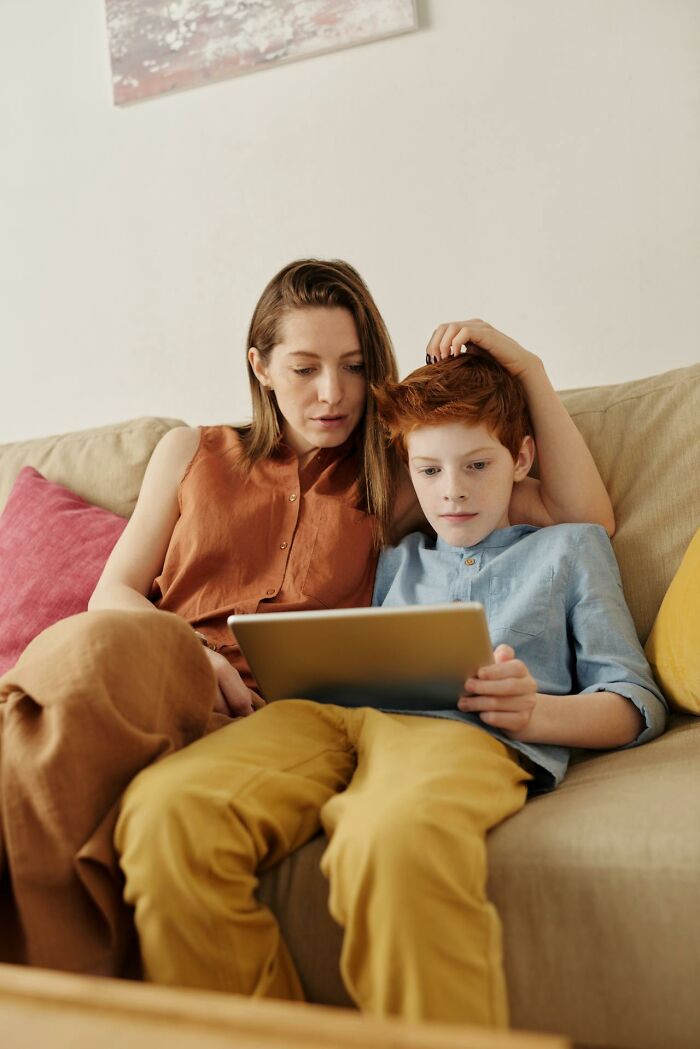 Mother and son on a couch reading a tablet together, reacting to a rained frogs story