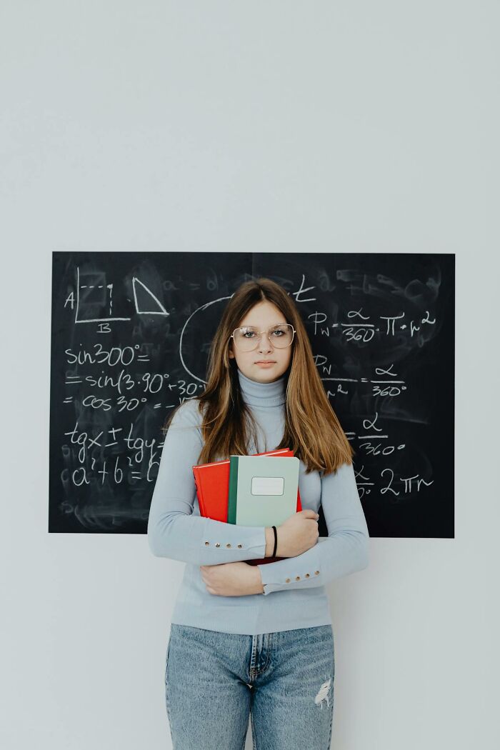 Student with glasses holding notebooks in front of a math chalkboard, representing creepiest displays of intelligence