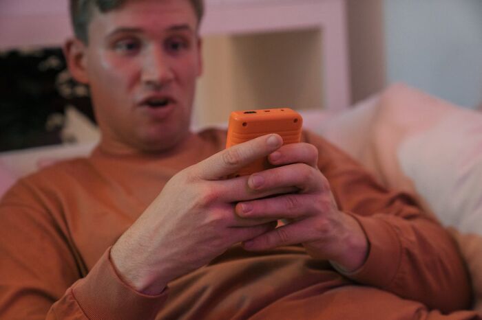 A young man on a couch with a shocked expression, looking at his phone after an accidental text caused panic.