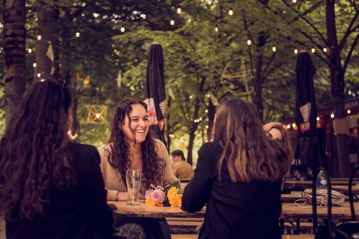 Four women chatting and laughing outdoors at a wooden table, enjoying cheat codes to make everyday life easier.