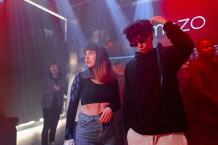 Young people dancing and socializing under colorful lights inside a vibrant nightclub party scene.