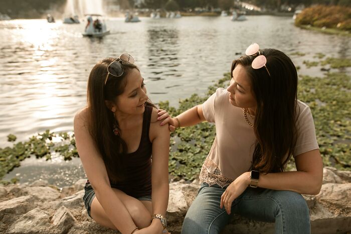 Two women sitting by a lake, sharing life tips and cheat codes to make everyday life easier in a relaxing outdoor setting.
