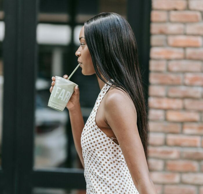 Woman with long hair drinking smoothie outdoors, representing things women do to feel safer while living alone.