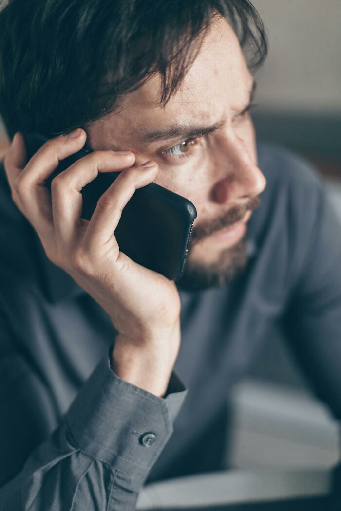 Man in a gray shirt on a phone call, showing stress and exhaustion during a chaotic 3 AM night shift at work.