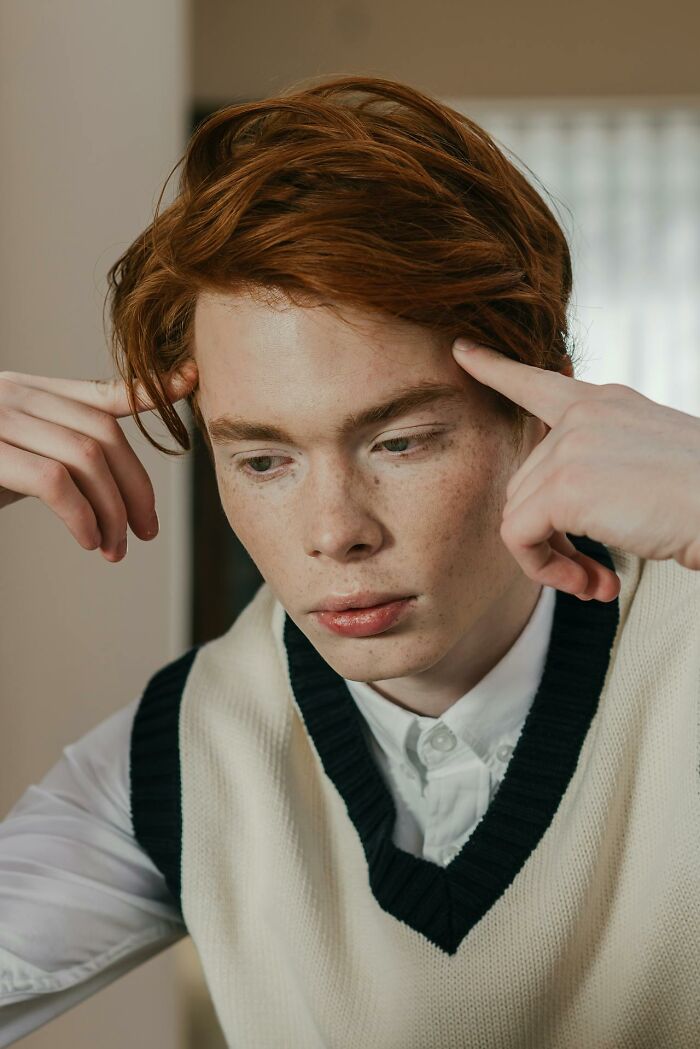Young man with red hair and freckles, wearing a white shirt and vest, looking thoughtful and detached from reality.