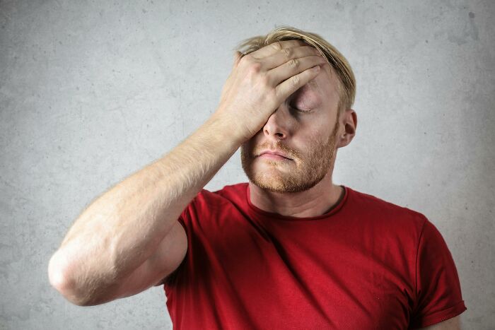 Man in red shirt with hand on forehead looking stressed, reflecting on biggest family secrets shared by 32 people