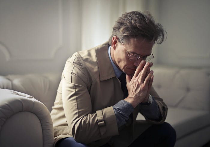 Man sitting on a couch with hands clasped near face, showing guilt and sadness amid messy divorce and distancing from daughter.