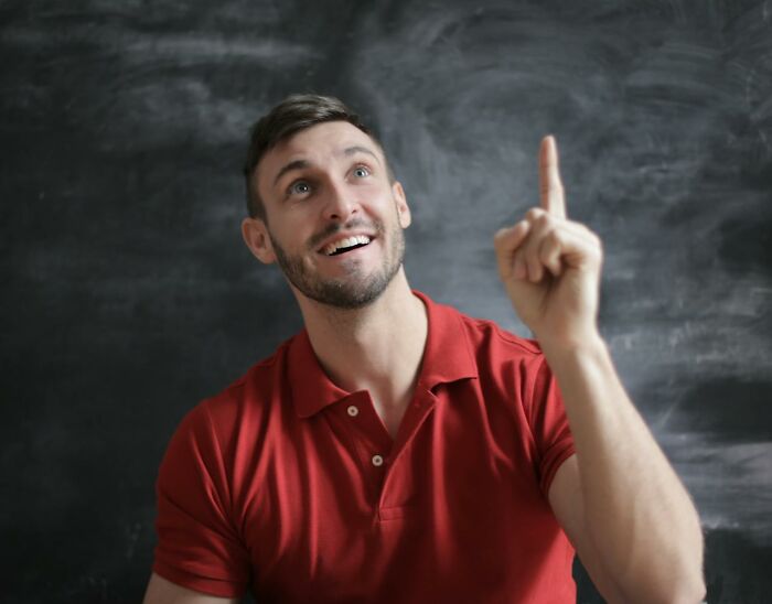 Man in red polo smiling and pointing upward against chalkboard, representing creepiest displays of intelligence.