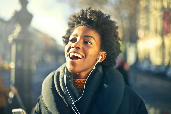 Young woman outdoors enjoying music with earphones on, smiling and showing passion for timeless music questions.