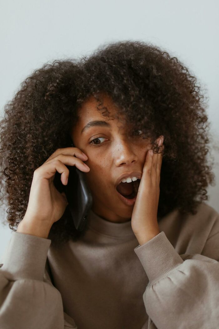 Woman with curly hair expressing shock while on a phone call related to 3 AM chaos during the night shift work