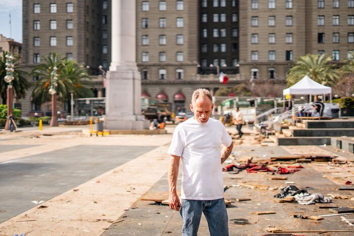 Man in white shirt standing alone looking down in a city plaza, depicting shock and adjustment after getting out of prison