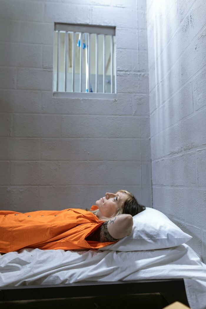 Woman in an orange prison uniform lying on a bed in a cell, reflecting on things that shocked people after prison release.