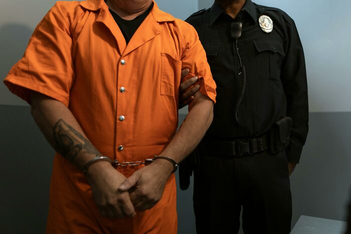 Inmate in orange prison uniform with handcuffs escorted by prison officer illustrating life in prison misconceptions.