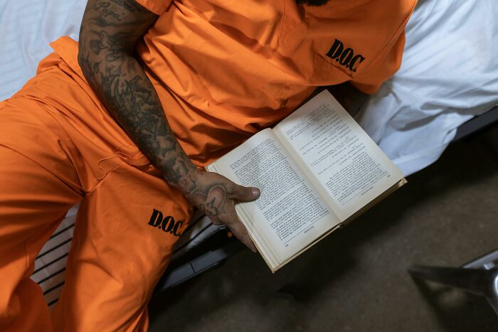 Inmate wearing orange prison uniform reading a book, illustrating life in prison misconceptions and realities.