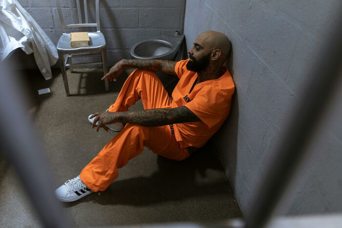 A prisoner in an orange jumpsuit sitting on the floor of a small cell, illustrating life in prison misconceptions.