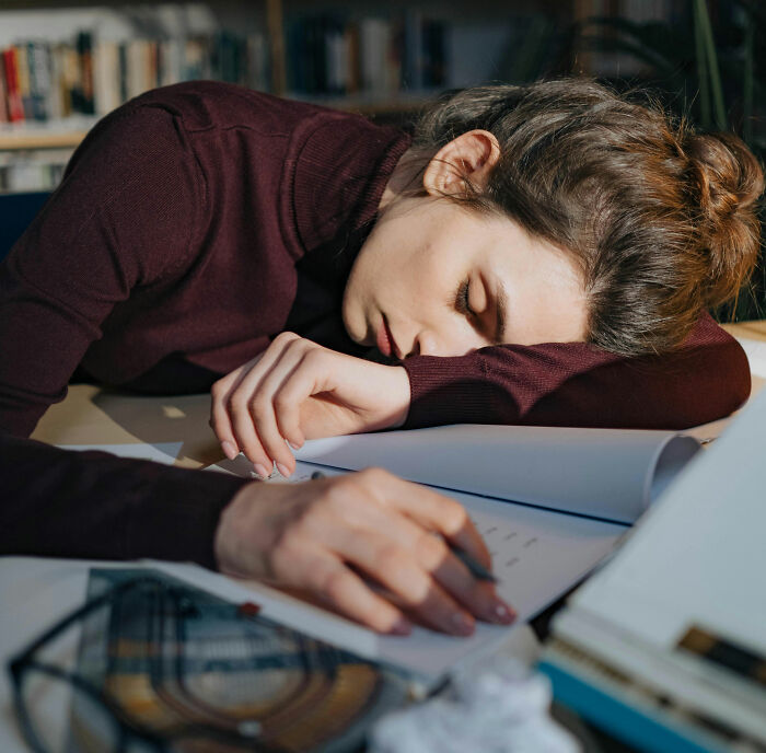 Young woman exhausted and sleeping at desk surrounded by papers, illustrating coworkers acting so unhinged at work stories.