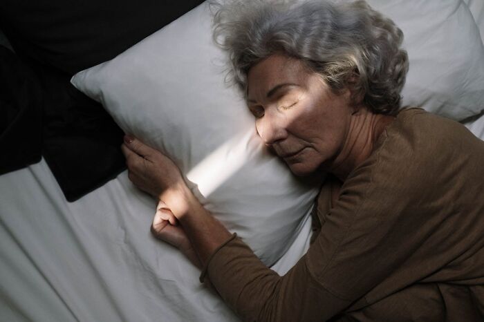 Elderly woman sleeping in bed with light across her face, hospital workers story context