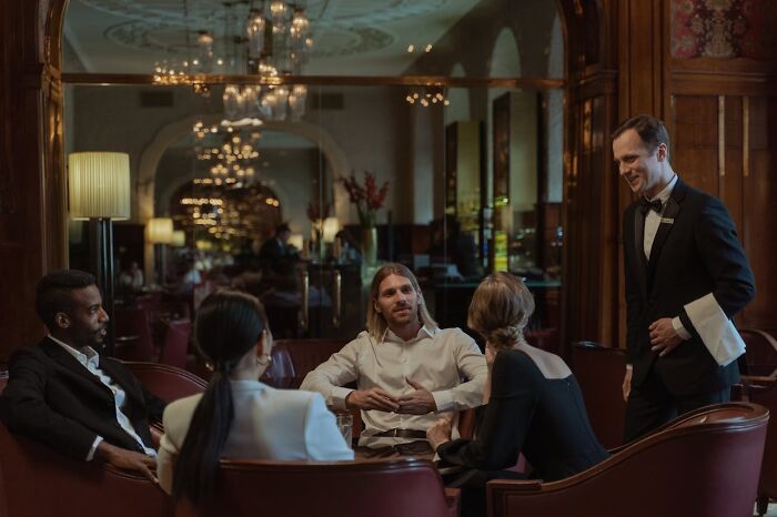 A group of rich people in luxurious attire sitting in an opulent room, showing how far from reality they are.