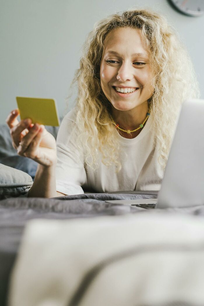 Smiling woman on bed holding a card beside laptop, illustrating creepiest displays of intelligence online