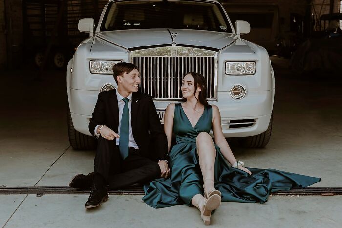 Young couple dressed elegantly sitting in front of a luxury car, illustrating rich people far from reality.