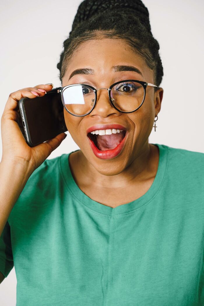 Surprised woman in green shirt and glasses holding phone, reacting excitedly to It Rained Frogs story