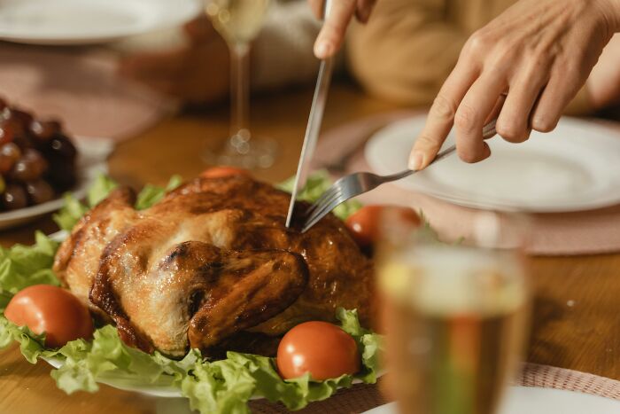 Person carving a roasted chicken on a plate with lettuce and tomatoes, illustrating rich people out of pocket comments.