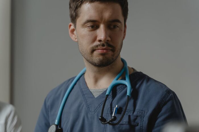 Hospital workers: male clinician in blue scrubs with stethoscope, looking solemn in clinical setting
