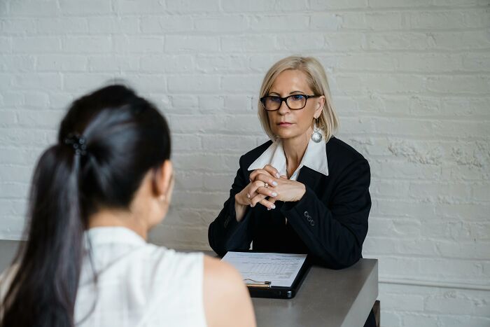 Woman in glasses conducting a serious coworker interview in an office setting, discussing unhinged behavior cases.