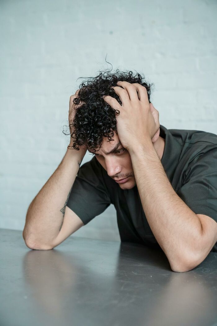 A young man with curly hair looks distressed sitting at a table, reflecting on things that shocked people after prison.
