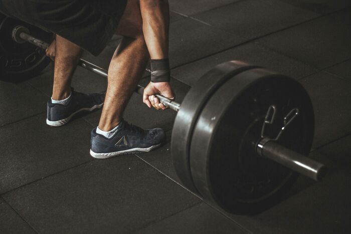 Person gripping heavy barbell, preparing to lift weights in gym, illustrating strength and determination amid workplace challenges.