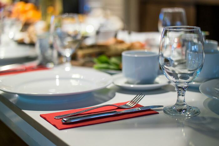 Table set with glass, white plate, cup, fork, and knife on a red napkin for an upscale dining experience.