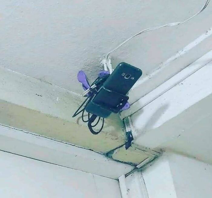 Smartphone charging rigged to ceiling with clothespins and wires, showcasing funny Eastern European experience humor.