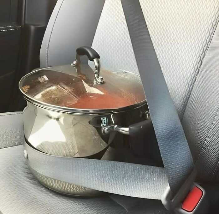 Large cooking pot with lid filled with food secured by a seatbelt on a car seat, capturing Eastern European experience humor.