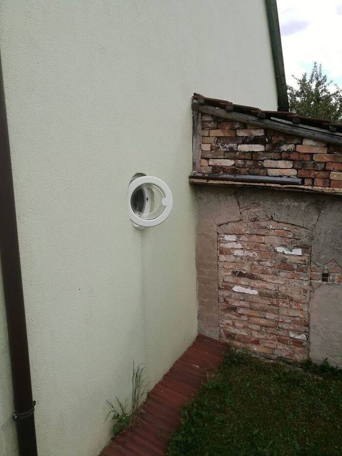 Washing machine door oddly installed on house exterior wall, capturing a funny Eastern European experience moment.
