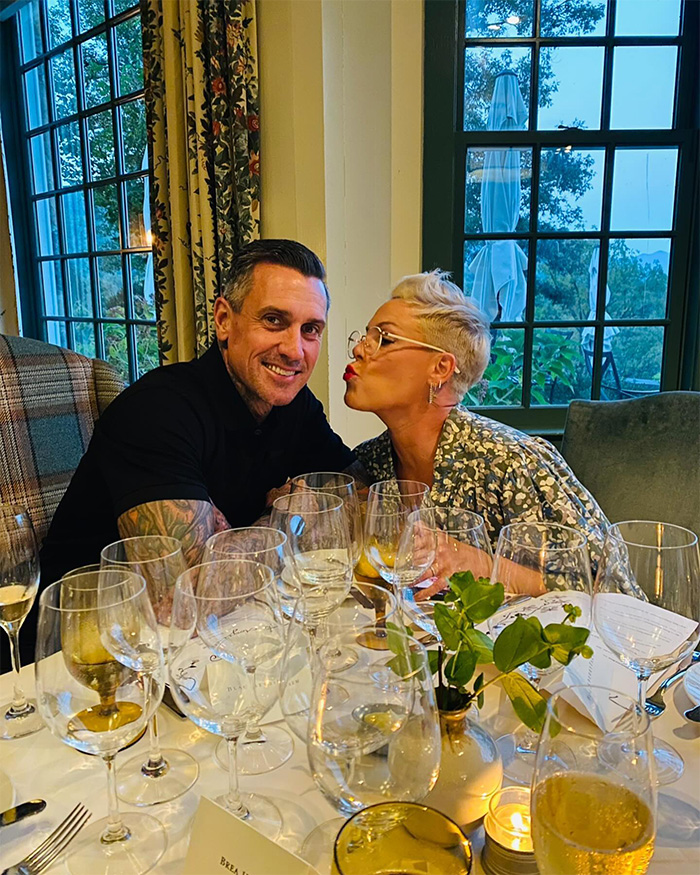 Pink and a companion seated at a table with multiple wine glasses, sharing a joyful moment indoors.