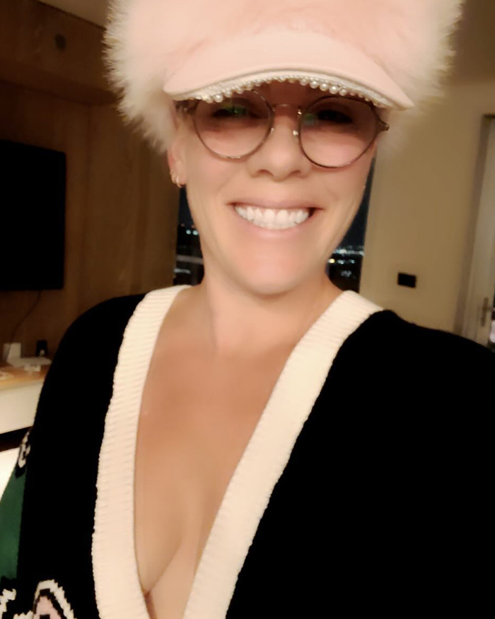 Pink smiling in a hat and glasses, breaking silence after spending New Year&rsquo;s Eve alone in hospital, indoors selfie.