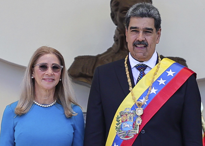 Venezuelan leader wearing presidential sash standing next to a woman in blue, related to Pentagon pizza spike theory during attack.