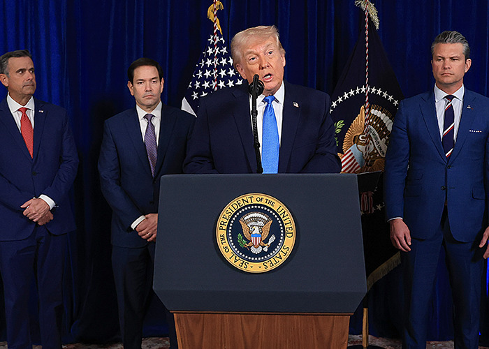 Former President Trump speaking at a podium with the presidential seal, flanked by men in suits and flags behind them.
