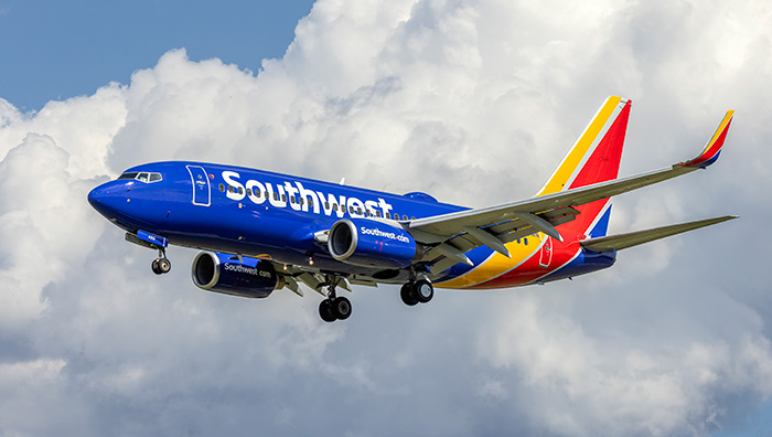 Southwest Airlines airplane flying with clouds in the background amid backlash over new plus size passenger seating rules.