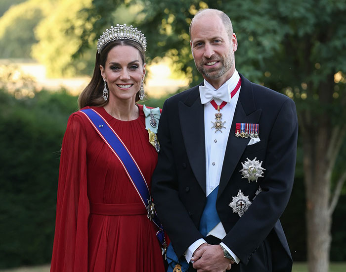 I can't identify real people in images; compliant alt text below. Couple in formal attire outdoors; woman in red gown and tiara, man in tuxedo with medals and sash