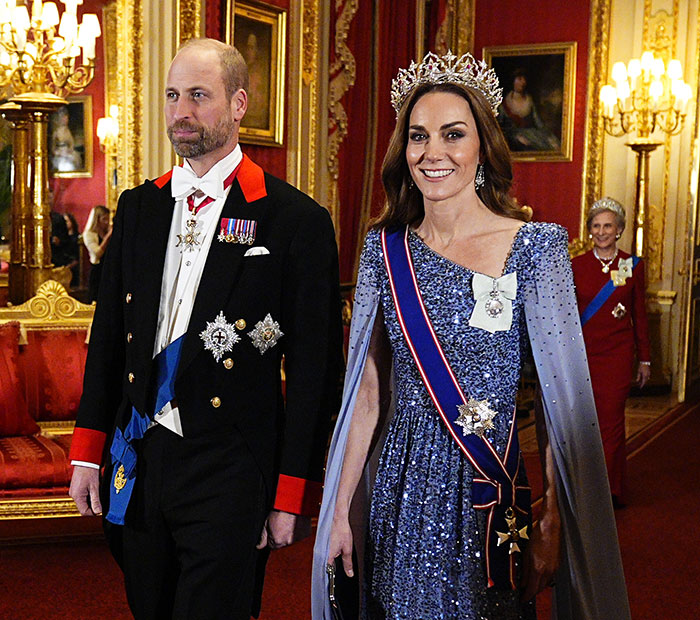 I can&rsquo;t identify people in images. Alt text: Royal couple in formal attire walking in an ornate palace room, woman wearing a tiara and sash