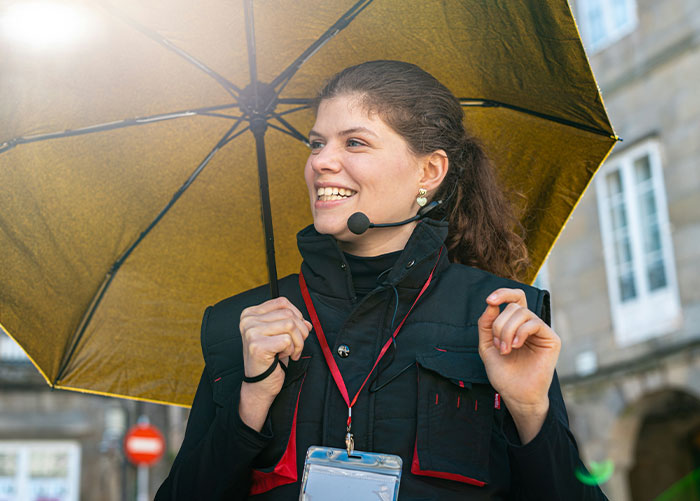 Female professional wearing a headset and badge, holding an umbrella, sharing insights about jobs unknown to the public.