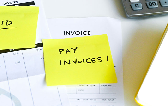 Sticky notes with pay invoices reminders on documents near calculator, illustrating professionals jobs insight.