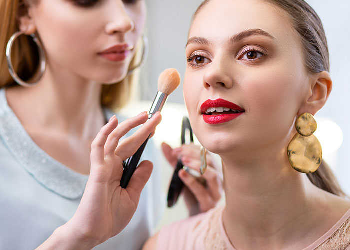 Makeup artist applying powder to model’s face, illustrating insights professionals share about their jobs unseen by the public.