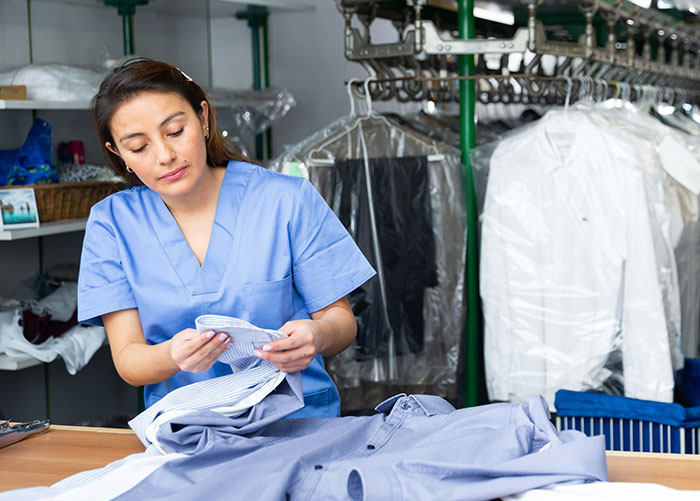 Woman in blue uniform inspecting clothes in a dry cleaning shop, illustrating professionals' behind-the-scenes job insights.