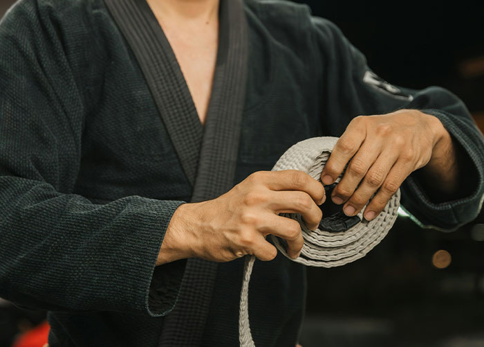 Person in a black martial arts uniform holding and preparing a white belt, illustrating professionals sharing job insights.