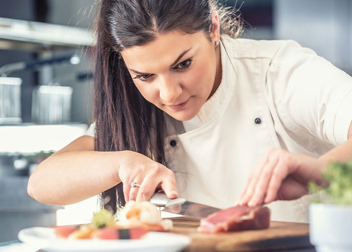 Female professional chef carefully preparing food in a kitchen, highlighting what the general public doesn’t know about jobs.
